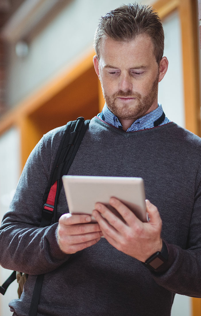 In a hallway, a man stands with a tablet, appearing to read or interact with the device thoughtfully.