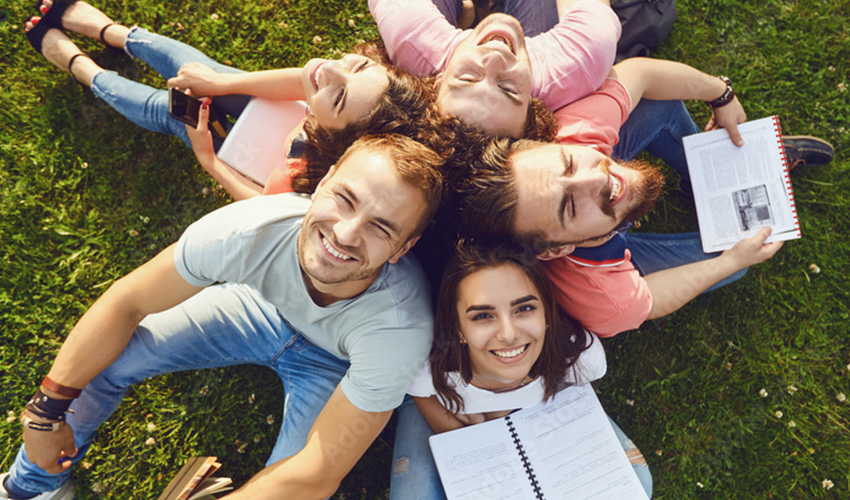 A group of students relaxing on the grass, surrounded by open books, enjoying a sunny day outdoors.