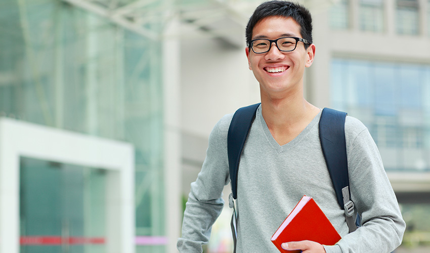 A CSUN student with glasses and a backpack smiles warmly, embodying a spirit of enthusiasm and academic engagement.