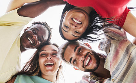 A diverse group of international students smiles brightly while looking down at the camera, radiating joy and camaraderie.