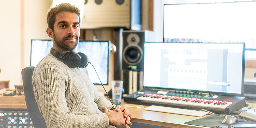 A music producer sitting at a desk with headphones and a keyboard.